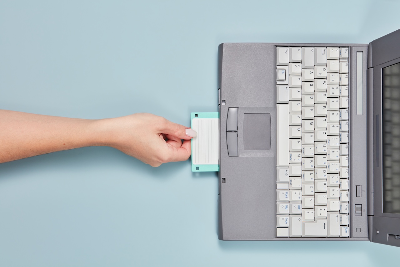 Persoon steekt diskette in oude laptop, om archief te lezen.